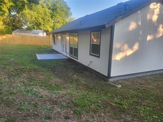 view of side of home with french doors, a yard, a shingled roof, and fence