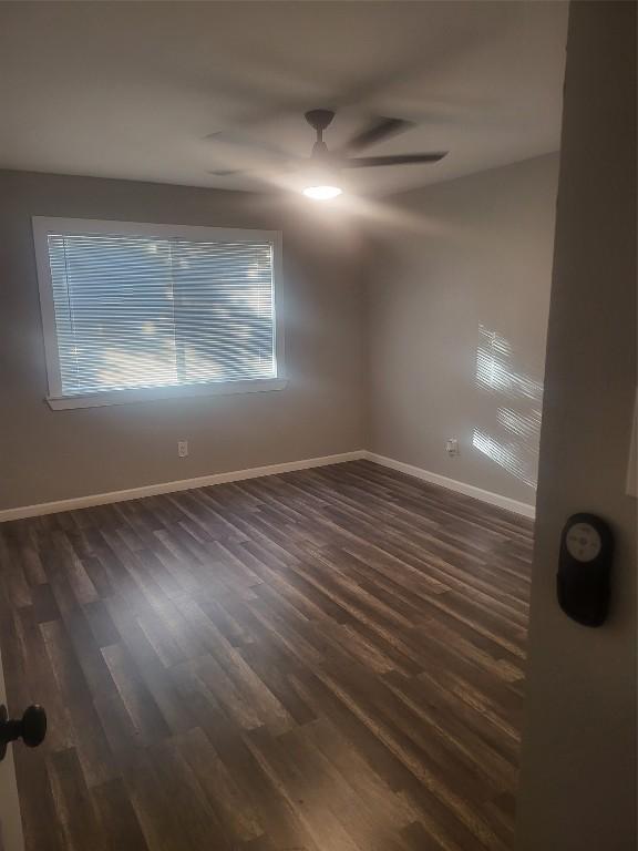 empty room with a ceiling fan, dark wood-type flooring, and baseboards