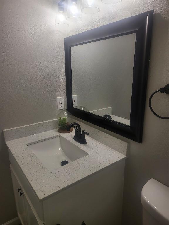 half bath featuring toilet, vanity, and a textured wall