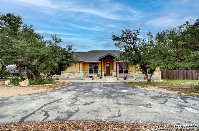 view of front of home with aphalt driveway, stone siding, and fence