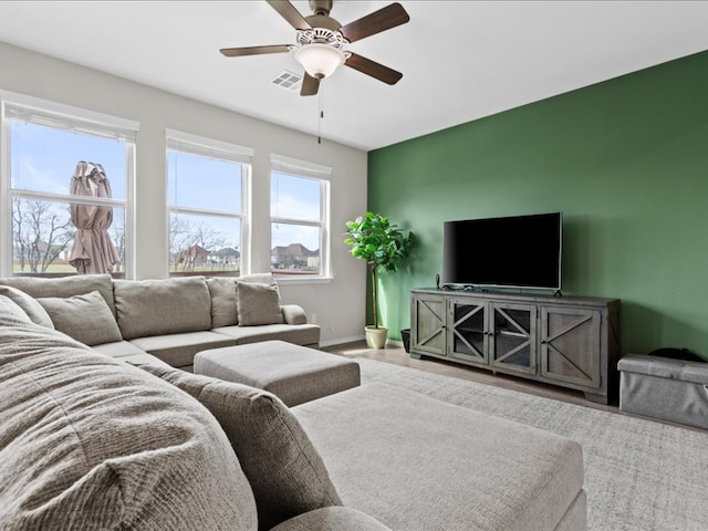 living area featuring visible vents, baseboards, an accent wall, and ceiling fan