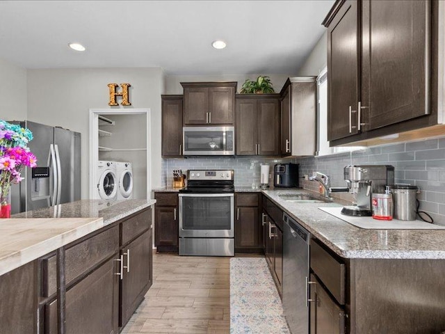 kitchen featuring washer and clothes dryer, a sink, stainless steel appliances, light wood-style floors, and dark brown cabinetry