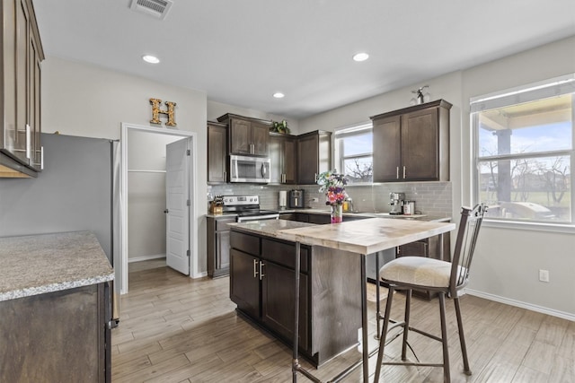 kitchen featuring visible vents, decorative backsplash, dark brown cabinetry, appliances with stainless steel finishes, and a kitchen bar