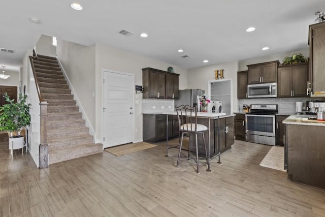 kitchen with visible vents, dark brown cabinets, a center island, appliances with stainless steel finishes, and washer and dryer