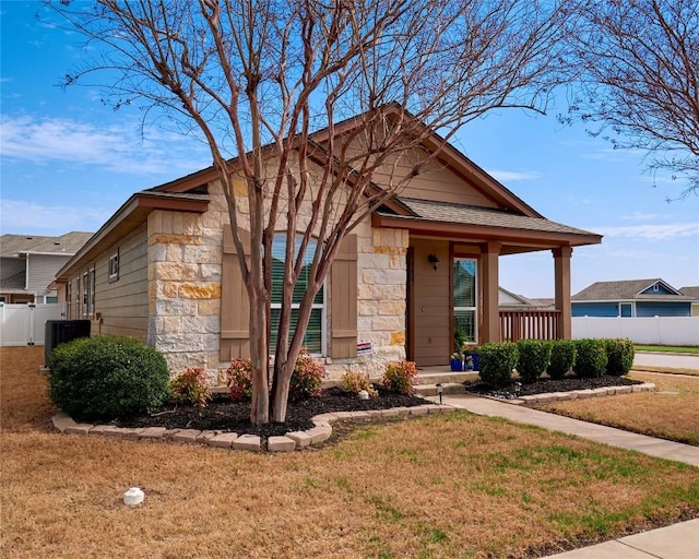 view of front of house featuring a front lawn, central air condition unit, fence, and stone siding