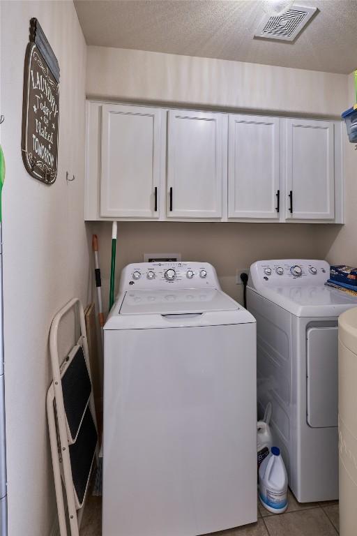 laundry room featuring washing machine and clothes dryer, visible vents, cabinet space, and tile patterned flooring