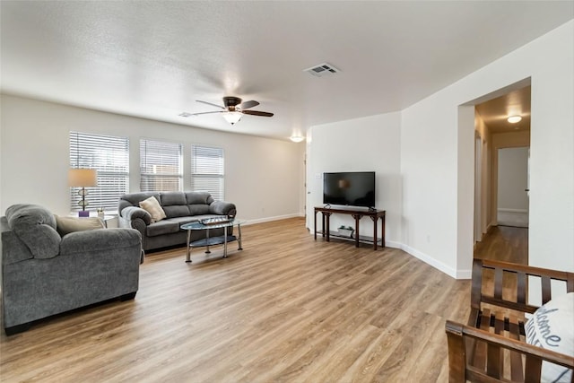 living area featuring light wood-type flooring, visible vents, a ceiling fan, a textured ceiling, and baseboards