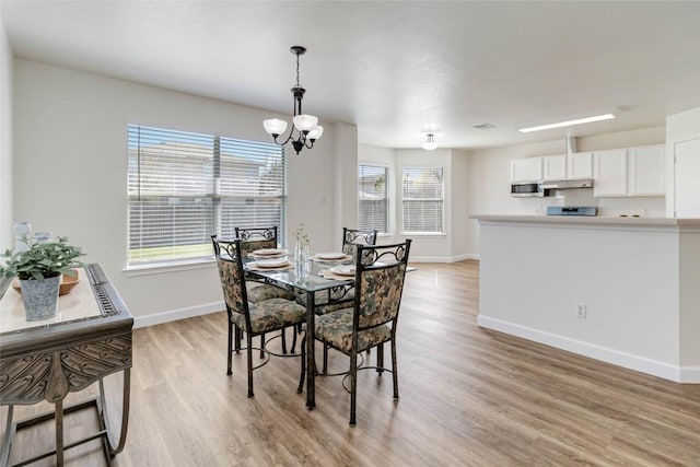 dining room featuring light wood-type flooring, baseboards, and a notable chandelier