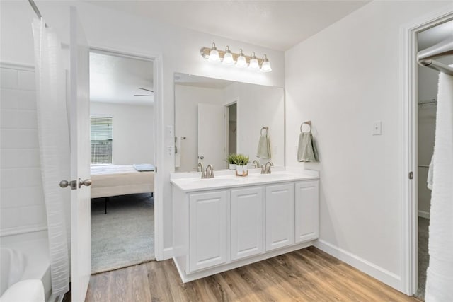 ensuite bathroom with double vanity, wood finished floors, baseboards, and a sink