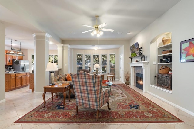 living room with built in features, a ceiling fan, light tile patterned floors, ornate columns, and a fireplace with flush hearth