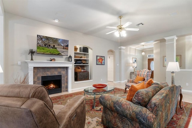 living area featuring visible vents, built in shelves, ceiling fan, a fireplace, and ornate columns