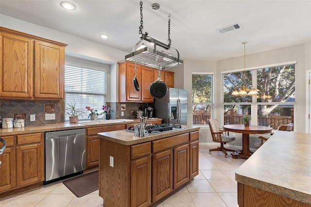 kitchen featuring light tile patterned floors, brown cabinets, a sink, appliances with stainless steel finishes, and tasteful backsplash