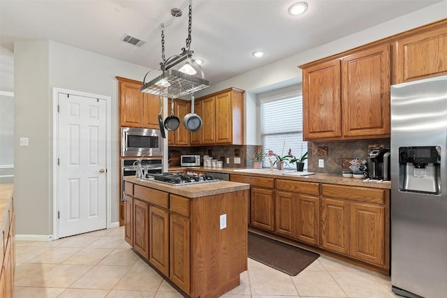 kitchen with brown cabinetry, visible vents, a sink, appliances with stainless steel finishes, and a center island