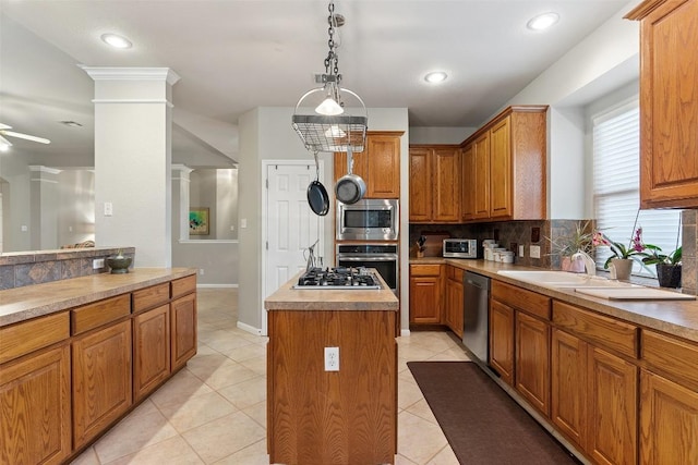 kitchen with brown cabinetry, appliances with stainless steel finishes, a kitchen island, and decorative columns