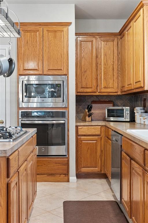 kitchen with tasteful backsplash, a toaster, light tile patterned floors, appliances with stainless steel finishes, and brown cabinetry