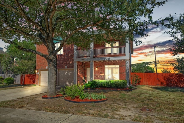 view of front of home featuring a balcony, fence, concrete driveway, a garage, and brick siding