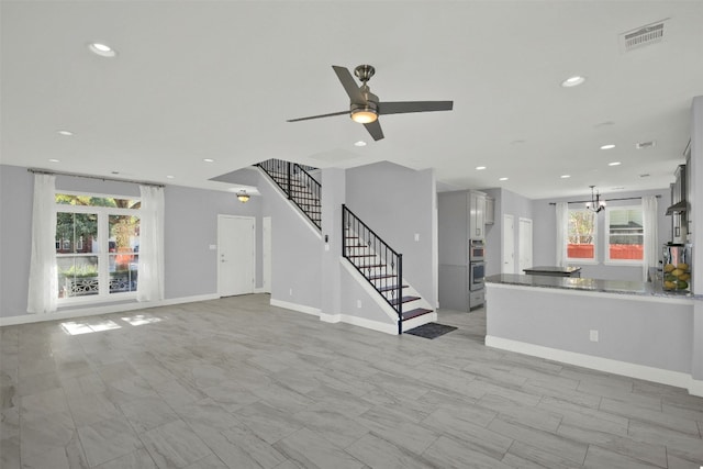 unfurnished living room featuring visible vents, baseboards, recessed lighting, stairs, and ceiling fan with notable chandelier