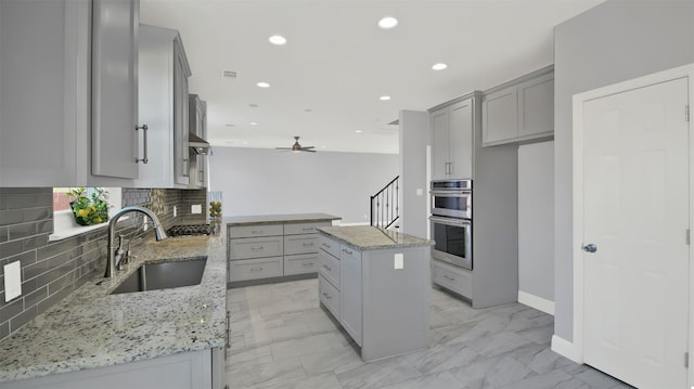 kitchen featuring marble finish floor, gray cabinets, a sink, light stone counters, and stainless steel appliances