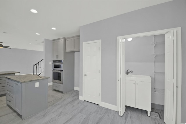 kitchen with a ceiling fan, a kitchen island, recessed lighting, gray cabinets, and double oven