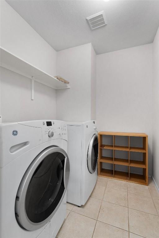 clothes washing area featuring light tile patterned floors, visible vents, washer and dryer, and laundry area