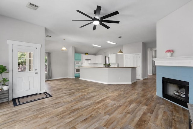 living area with visible vents, a tiled fireplace, lofted ceiling, light wood-style floors, and a ceiling fan