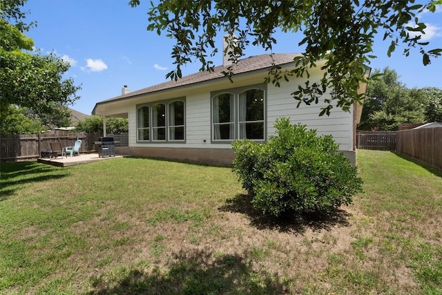 back of house with a fenced backyard, a patio area, a chimney, and a yard