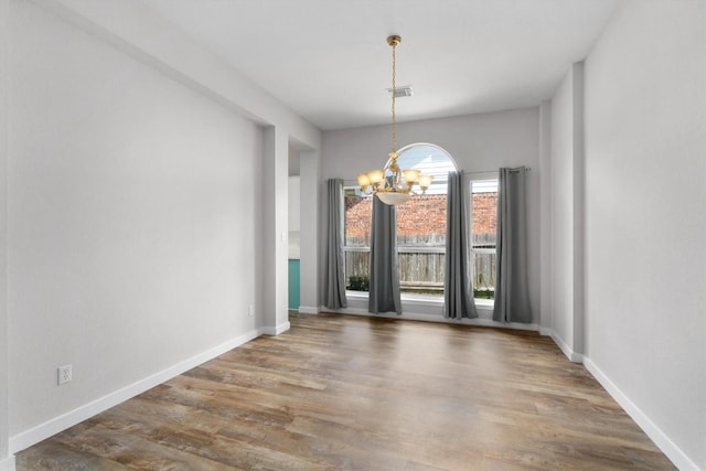 unfurnished dining area featuring baseboards, wood finished floors, visible vents, and a chandelier