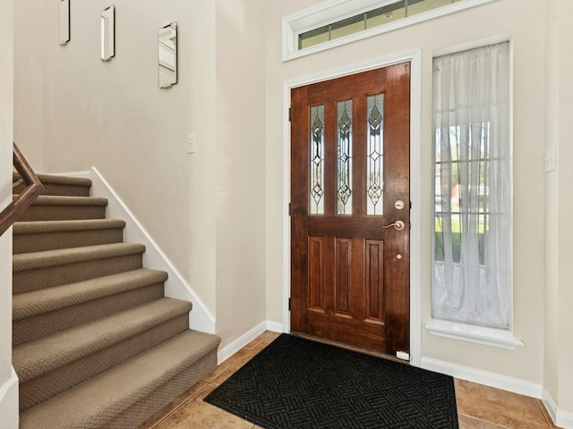 foyer entrance with baseboards, plenty of natural light, tile patterned flooring, and stairway