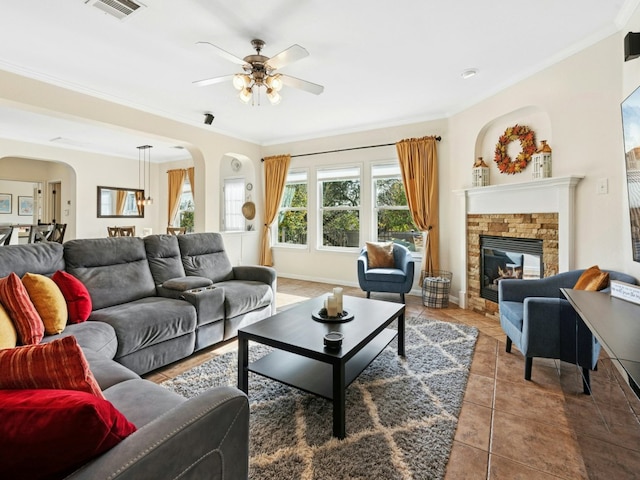 living area with a stone fireplace, tile patterned floors, visible vents, and ornamental molding