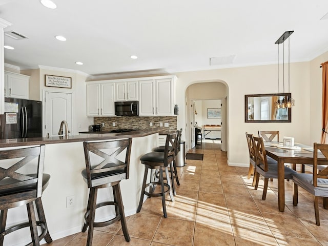 kitchen with dark countertops, stainless steel microwave, a breakfast bar, freestanding refrigerator, and arched walkways