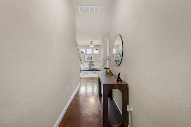 hallway with visible vents, finished concrete flooring, baseboards, and a textured wall