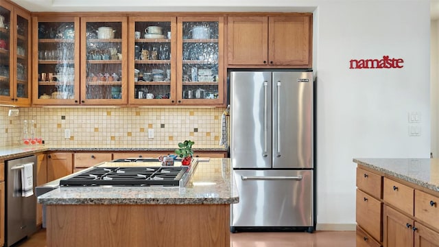 kitchen with stainless steel appliances, light stone countertops, tasteful backsplash, and a center island