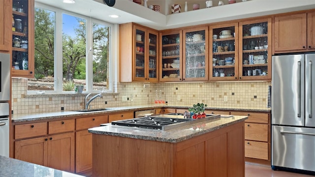 kitchen featuring a sink, a kitchen island, appliances with stainless steel finishes, glass insert cabinets, and light stone countertops