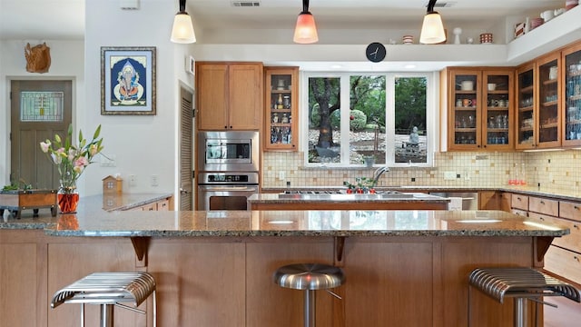 kitchen with glass insert cabinets, light stone counters, decorative backsplash, appliances with stainless steel finishes, and a kitchen breakfast bar