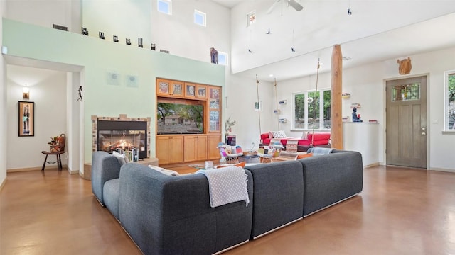 living area with visible vents, finished concrete flooring, baseboards, a lit fireplace, and a high ceiling