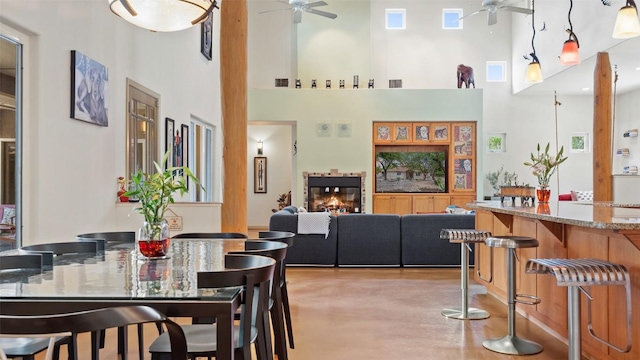 dining space with a glass covered fireplace, visible vents, a ceiling fan, and a towering ceiling