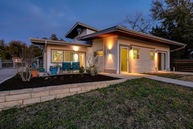 view of front of house with concrete block siding, a patio area, and fence