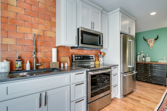 kitchen with light wood-type flooring, a sink, backsplash, stainless steel appliances, and white cabinets