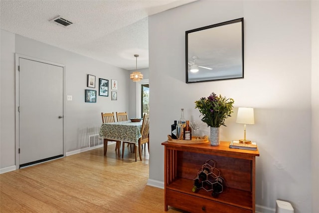 foyer entrance with visible vents, light wood-style flooring, a textured ceiling, and baseboards