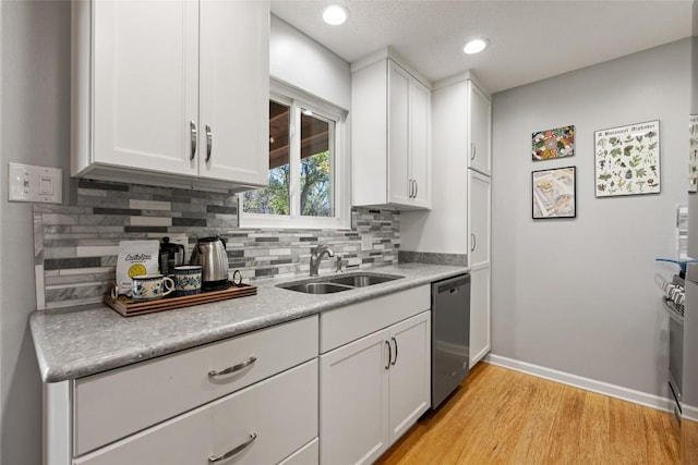 kitchen with white cabinetry, a sink, stainless steel dishwasher, light wood-type flooring, and backsplash