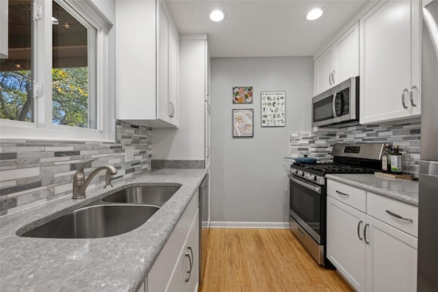 kitchen with light wood-type flooring, light stone counters, appliances with stainless steel finishes, white cabinetry, and a sink