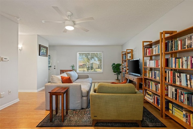 living room with a ceiling fan, wood finished floors, baseboards, and a textured ceiling