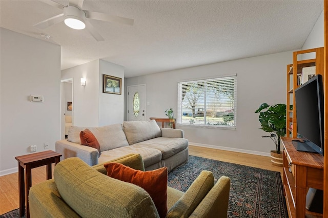 living area with a textured ceiling, wood finished floors, baseboards, and ceiling fan