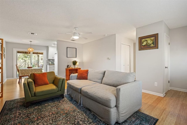 living area with visible vents, light wood-style flooring, a textured ceiling, baseboards, and ceiling fan