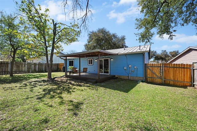 back of house featuring a standing seam roof, a gate, a fenced backyard, a yard, and metal roof