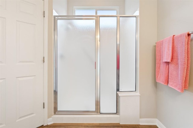 full bathroom with wood finished floors, baseboards, and a stall shower