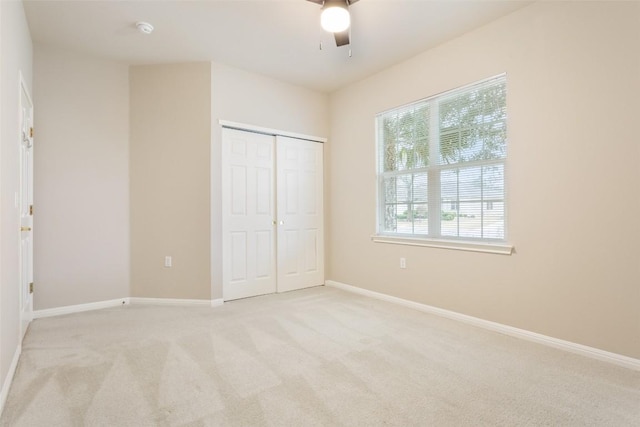 unfurnished bedroom featuring a ceiling fan, light colored carpet, baseboards, and a closet