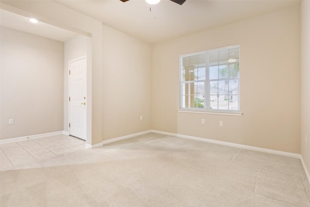 empty room featuring a ceiling fan, light tile patterned floors, light colored carpet, and baseboards