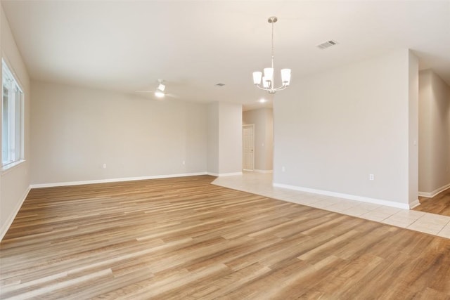 empty room with ceiling fan with notable chandelier, baseboards, visible vents, and light wood finished floors