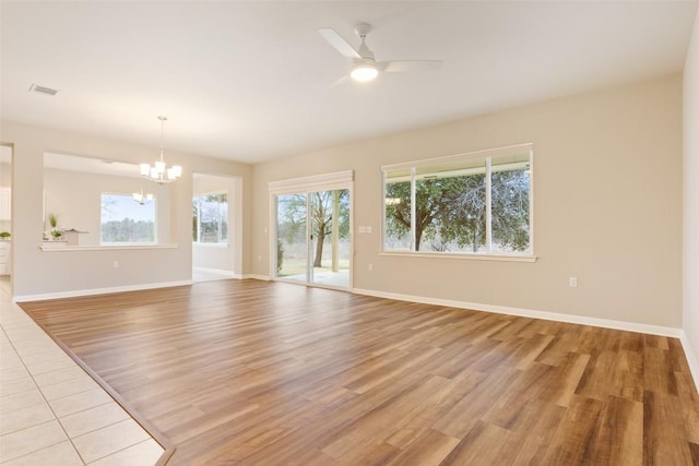 unfurnished living room with light wood-style flooring, ceiling fan with notable chandelier, visible vents, and baseboards